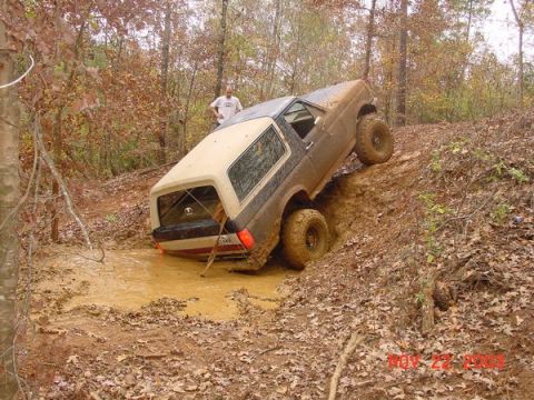 1989 Ford Bronco - A 1989 Ford Bronco is stuck in a muddy ditch off-road, with a person standing nearby.