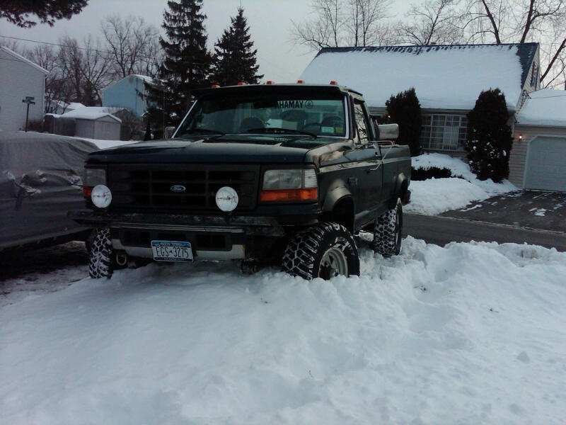 Front view of a 1996 Ford F-250 stuck in deep snow. It has large off-road tires and a front bumper with auxiliary lights