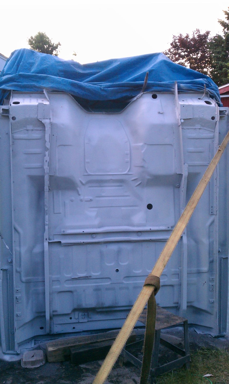 Vehicle frame upside down, covered by a blue tarp. A yellow strap is attached