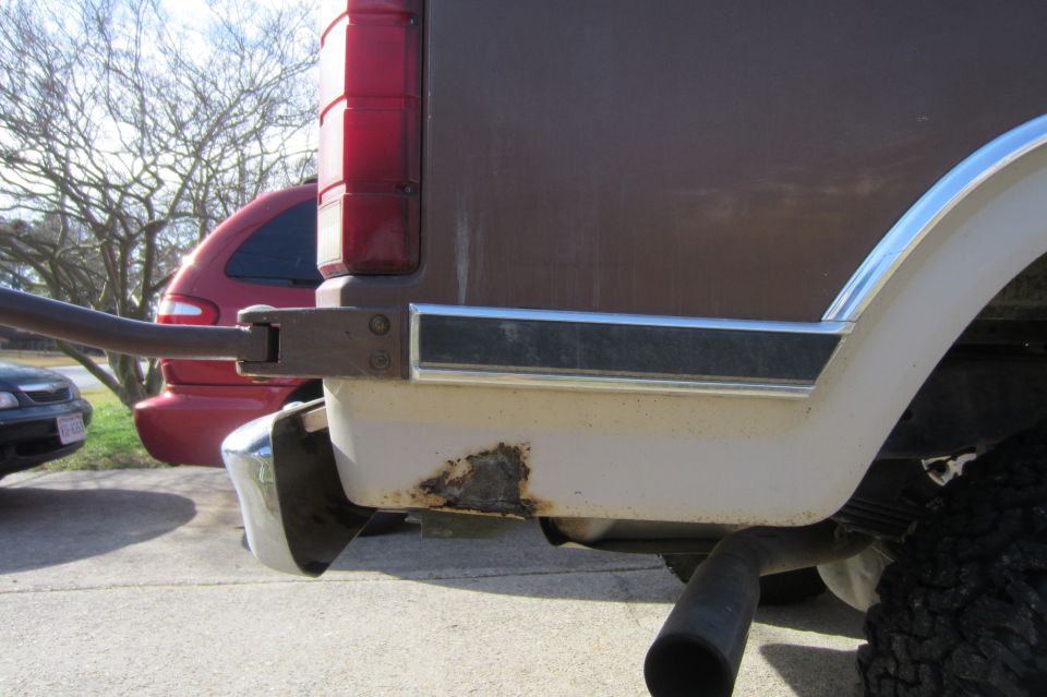 Rust hole on lower rear quarter panel of brown and white SUV near taillight and bumper