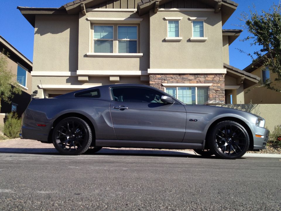 Gray 2013 Ford Mustang parked in front of a house. It has black rims and a '5.0' badge on the fender