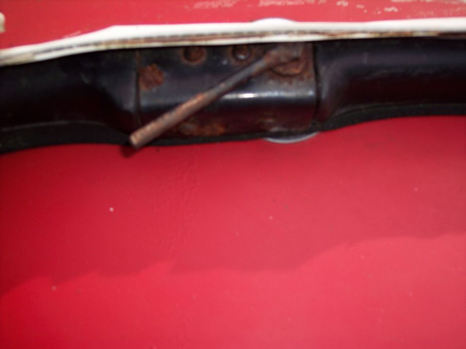 Close-up of a rusty metal rod attached to a black bracket, set against a red background