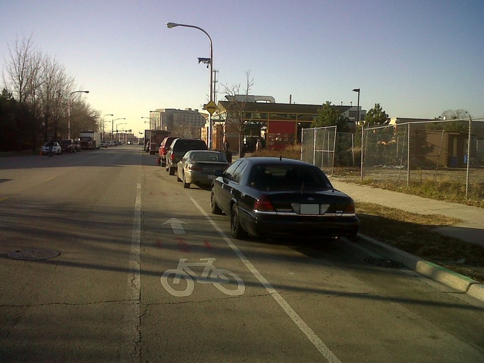 Black sedan parked on street next to a bike lane, with other cars in the background