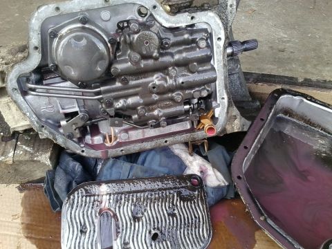 1985 Chevrolet Blazer - A disassembled automatic transmission, showing the internal components, filter, and pan with purple transmission fluid.