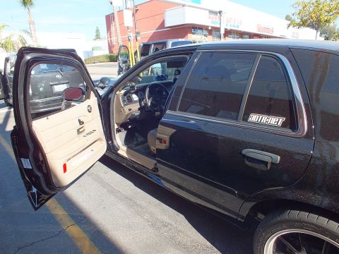 2003 Ford Crown Victoria - Open driver door of a black Crown Victoria revealing tan seats and dash, AUTR-DEF rear quarter glass decal