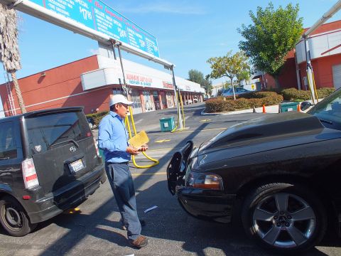 2003 Ford Crown Victoria - Attendant with clipboard stands between a black sedan and a boxy gray hatchback in a car-wash parking lot.