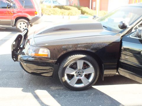 2003 Ford Crown Victoria - Close front-corner shot of a black car showing hood scoop, headlight area and gray alloy wheel.