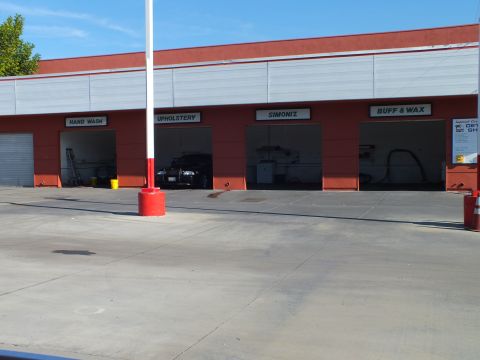2003 Ford Crown Victoria - Four open detail bays with overhead signage on a red building beside a red pole and concrete apron.