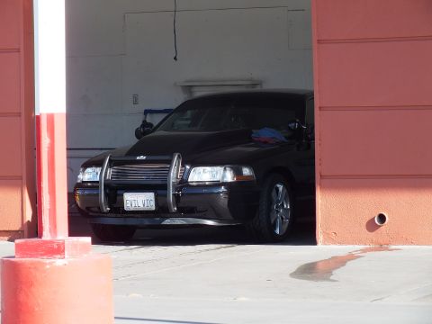 2003 Ford Crown Victoria - Front of a black sedan with chrome push bar and EVIL VIC plate seen through an open detail-bay door.