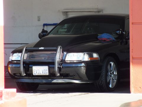 2003 Ford Crown Victoria - Close front view of a black sedan showing push bar, polished grille and EVIL VIC Crown Victoria plate.