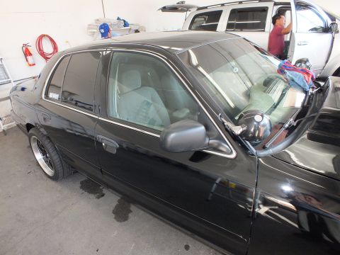 2003 Ford Crown Victoria - Driver profile of a black sedan with chrome trim and side mirror, parked in a detailing garage.