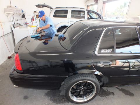2003 Ford Crown Victoria - Detailer kneels on a black sedan buffing the deck lid as another worker tends an SUV in the bay.