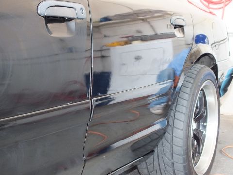 2003 Ford Crown Victoria - Close shot of a black car's rear door and fender showing polish reflections and a chrome-lip wheel.