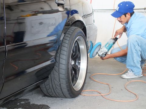 2003 Ford Crown Victoria - Detailer uses a blue rotary buffer on the rear quarter of a black sedan with a chrome-lip alloy wheel.