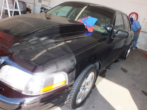 2003 Ford Crown Victoria - Front corner of a black sedan parked in a shop bay, worker with air hose in background