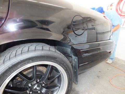 2003 Ford Crown Victoria - Rear fender and fuel filler door of black sedan above a black alloy wheel, worker behind