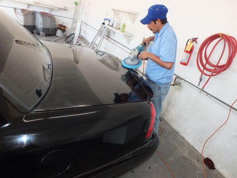 2003 Ford Crown Victoria - Technician polishing the rear deck of a black sedan with a rotary buffer in a garage