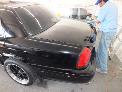 2003 Ford Crown Victoria - Black sedan rear three-quarter with glowing red taillight while worker buffs the trunk