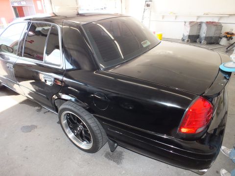 2003 Ford Crown Victoria - Lowered black sedan rear with trunk spoiler and dark alloy wheels parked in detailing bay