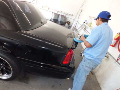2003 Ford Crown Victoria - Technician using a blue-pad polisher on the trunk lid of a black sedan near a taillight