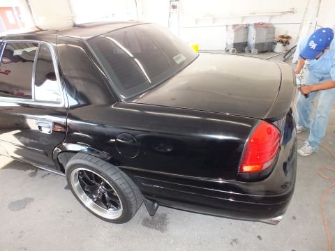 2003 Ford Crown Victoria - Lowered black sedan side profile with dark wheels while a worker polishes the rear deck