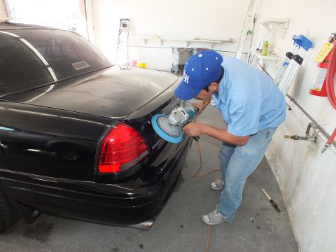 2003 Ford Crown Victoria - Technician in blue cap buffing the rear corner of a black sedan near the taillight