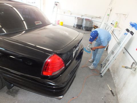 2003 Ford Crown Victoria - Technician polishing trunk of black sedan with rotary buffer near a folded ladder