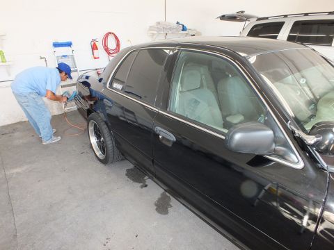 2003 Ford Crown Victoria - Technician polishing front fender of black sedan as white SUV sits behind in the bay