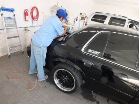 2003 Ford Crown Victoria - Technician polishing roof of black sedan bearing a window decal, alloy wheel in view