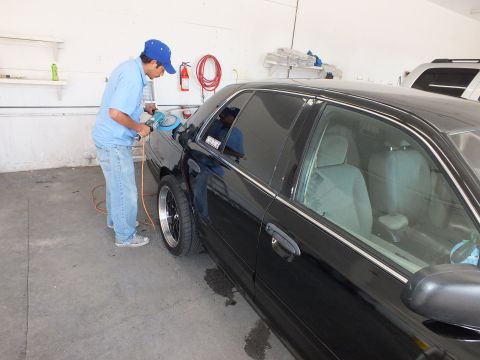 2003 Ford Crown Victoria - Technician using rotary buffer on front fender of a black sedan with tinted door glass