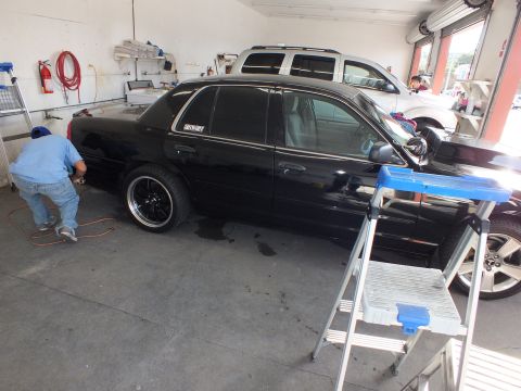2003 Ford Crown Victoria - Lowered black sedan full side view in detailing bay, worker crouched at the rear