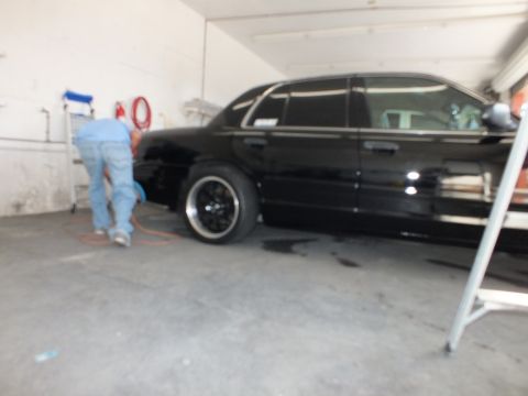 2003 Ford Crown Victoria - Out-of-focus side shot of a lowered black sedan in a garage bay with worker at the front