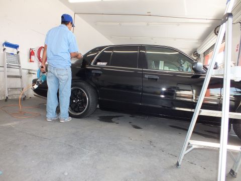 2003 Ford Crown Victoria - Technician in blue shirt applies window film to a lowered black Crown Victoria with black wheels.