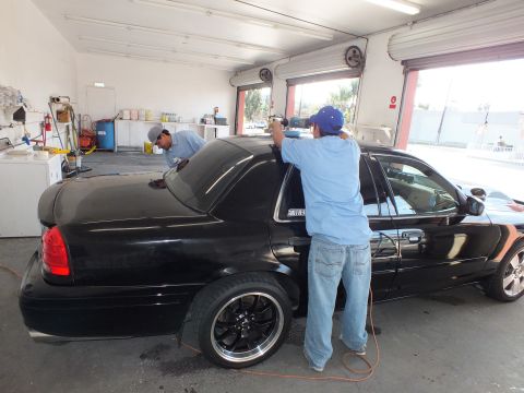 2003 Ford Crown Victoria - Rear quarter of a black sedan on black multi-spoke wheels while two techs install window film.