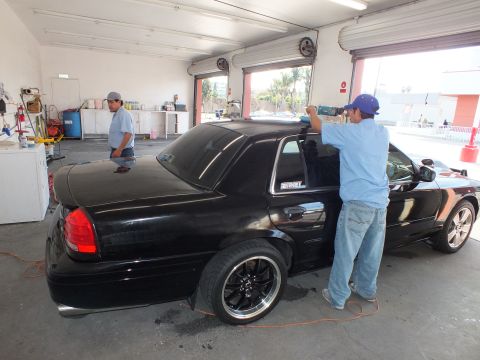 2003 Ford Crown Victoria - Lowered black sedan with chrome-lip black wheels gets rear glass tinted in a garage bay.