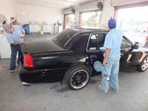 2003 Ford Crown Victoria - Rear quarter of black sedan on black wheels as a tech sprays application fluid for window film.
