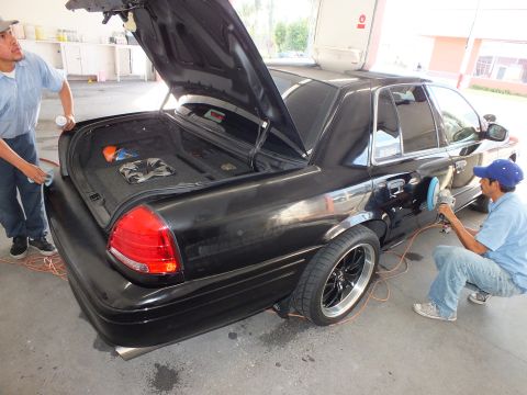 2003 Ford Crown Victoria - Trunk open on lowered black sedan, technician polishing the rear fender with an orange air line.