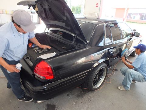 2003 Ford Crown Victoria - Open-trunk black sedan with red taillight as a second tech buffs the rear quarter panel.