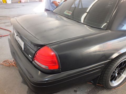 2003 Ford Crown Victoria - Sanded black trunk and quarter panel with a chrome GTI badge and chrome-lip wheel below.