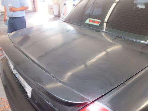 2003 Ford Crown Victoria - Dark gray trunk and rear glass with heavy buffing swirls and a worker standing at left.