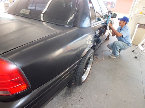 2003 Ford Crown Victoria - Worker crouches with a polisher at the rear door of a lowered black sedan in a shop bay.