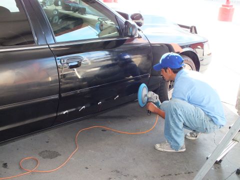 2003 Ford Crown Victoria - Crouching technician runs a rotary buffer with blue pad along the black sedan's front door.