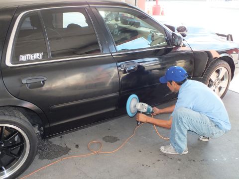 2003 Ford Crown Victoria - Worker polishes the rear fender of a black sedan wearing a chrome-spoke wheel in a garage.
