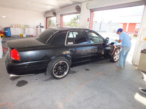 2003 Ford Crown Victoria - Full side profile of a lowered black sedan as a tech buffs the body with an orange air line.