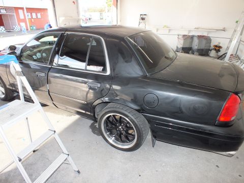 2003 Ford Crown Victoria - Lowered black sedan on chrome-lip black wheels parked beside a step ladder in a garage.