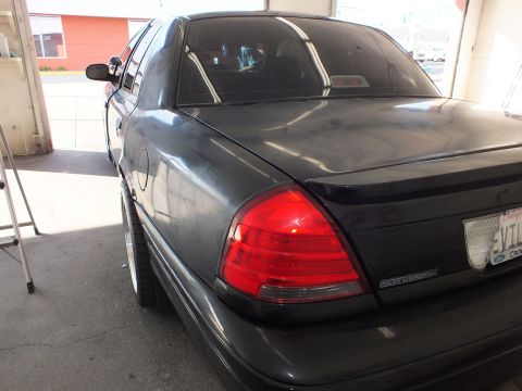 2003 Ford Crown Victoria - Lowered dark gray sedan on chrome wheels with EVIL VIC plate parked in an open garage bay.