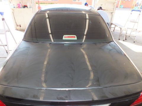 2003 Ford Crown Victoria - Wide rear view of a dark sedan trunk and back window showing buffing swirl marks.