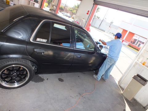 2003 Ford Crown Victoria - Technician applies window film to the front door of a lowered black sedan in an open bay.