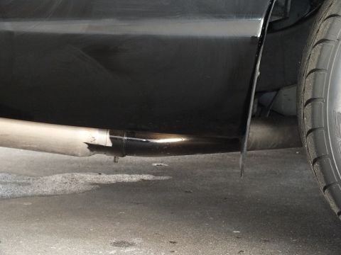 2003 Ford Crown Victoria - Close-up of a single chrome exhaust tip exiting beneath a black vehicle's rocker on a garage floor.
