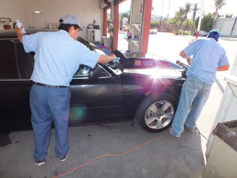 2003 Ford Crown Victoria - Detailers in blue shirts clean a black drop-top sedan inside an open garage bay.